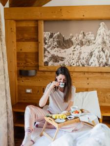 una mujer sentada en una cama bebiendo una taza de café en Hotel La Bussola, en Andalo