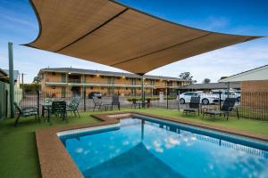a swimming pool with a large umbrella over it at Garden City Motor Inn in Wagga Wagga