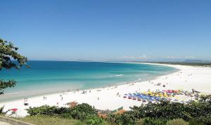 a beach with people and umbrellas and the ocean at Apartamento Sophia 1 in Arraial do Cabo