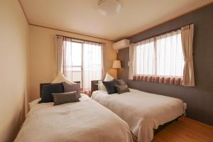 two beds in a room with two windows at Hyakuna Terrace in Nanjo