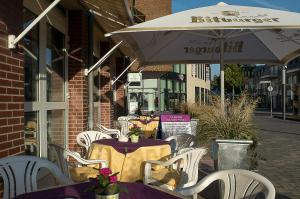 ein Café im Freien mit Tischen, Stühlen und einem Sonnenschirm in der Unterkunft Hotel Primula in Troisdorf