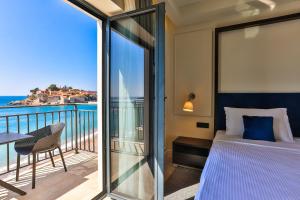 a bedroom with a bed and a balcony with the ocean at Hotel California by Aycon in Sveti Stefan