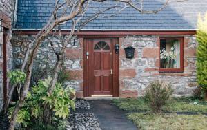 una casa in mattoni con una porta rossa e una finestra di Kerrowdown Cottage-Self Catering for 4 in the Highlands a Drumnadrochit