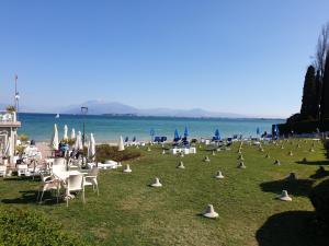 grupa krzeseł i parasoli na trawie w pobliżu wody w obiekcie Sun Lake Apartments w mieście Desenzano del Garda