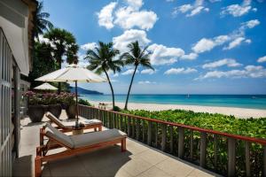 a balcony with chairs and an umbrella and the beach at The Surin Phuket in Surin Beach