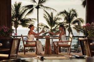 two women sitting at a table in front of a palm tree at The Surin Phuket - SHA Extra Plus in Surin Beach