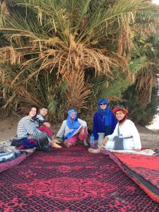 a group of people sitting on a rug in front of a tree at d'hôte Jnane-Dar Diafa in Tamgrout