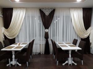 una sala da pranzo con due tavoli, sedie e tende di Орхідея a Romny