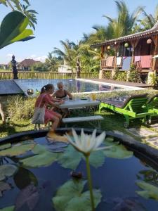 two girls sitting at a picnic table by a pool at Green Paddy Hostel & Villa in Ubud