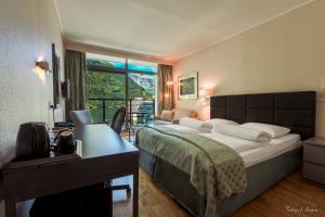 Cette chambre comprend un lit, un bureau et une fenêtre. dans l'établissement Havila Hotel Geiranger, à Geiranger