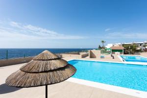 a straw umbrella sitting next to a swimming pool at Apartment direkt am Meer in Costa Del Silencio
