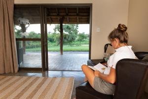 Una donna seduta su una sedia a leggere un libro di Senalala Safari Lodge a Klaserie Private Nature Reserve