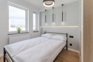 a bedroom with a bed with white sheets and two windows at Apartment Pink Flamingo by Renters in Międzyzdroje