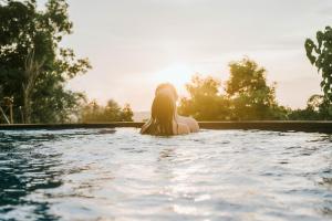 una mujer sentada en el agua en una piscina en Prasi Sunset Bungalows en Nusa Penida