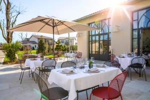 restauracja z białymi stołami i krzesłami oraz parasolem w obiekcie Hotel Clos Castel w mieście Casteljaloux