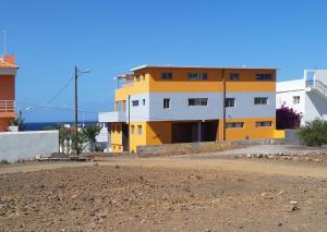a yellow and white building next to a dirt road at Casa Patio in Tarrafal
