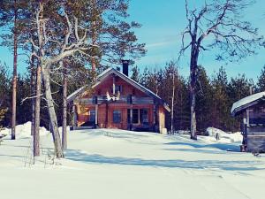una cabaña de madera en la nieve con árboles en Tarinatupa Simojärvi, en Impiö