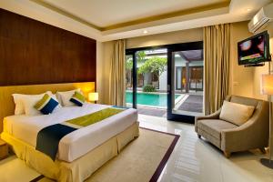 a bedroom with a bed and a chair and a tv at The Nibbana Villas in Seminyak