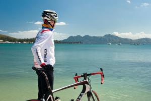a man standing next to a bike in front of the water at Cala Millor Garden Hotel - Adults Only in Cala Millor