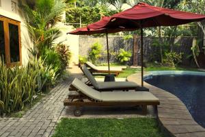 een groep ligstoelen en een parasol naast een zwembad bij Niramaya Villa in Seminyak