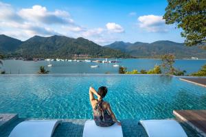 una mujer sentada en el borde de una piscina con vistas a un lago en Bhuvarin Resort, en Ko Chang