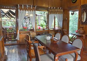 comedor con mesa, sillas y ventanas en Badjoeri Ethnic Wooden Homestay en Bandung