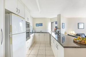 uma cozinha com armários brancos e um frigorífico branco em 2 Bedroom Ocean View - Alexandria Apartments -Alexandra Headland em Maroochydore