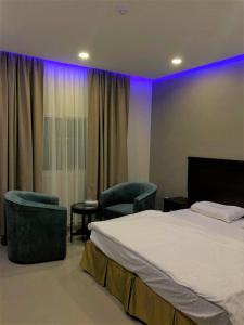 a bedroom with a bed and chairs and purple lights at White Beach Hotel Suites in Rabigh