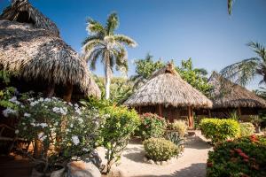 a group of huts with flowers and palm trees at Present Moment Retreat in Troncones