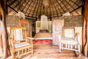 a bedroom with a bed and chairs in a hut at Present Moment Retreat in Troncones
