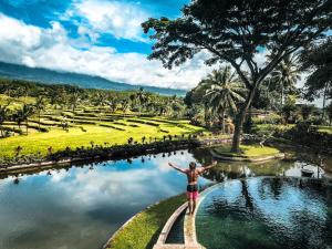 une femme debout sur un chemin en face d'un étang dans un parc dans l'établissement Ijen Resort and Villas - The Hidden Paradise, à Banyuwangi