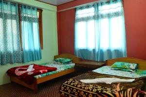 two beds in a room with blue curtains at VAMOOSE PARKHA SIKKIM in Rangli