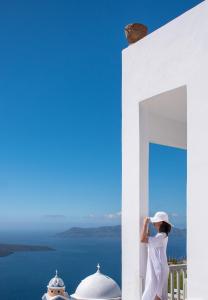 Una donna in piedi su un balcone che guarda l'oceano di Amelot Art Suites a Firà