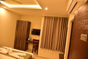 Habitación de hotel con cama, escritorio y TV. en Le Oak Inn, en Mysore