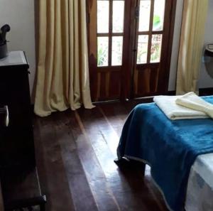 a bedroom with a bed with a blue blanket and two windows at Jardim das orquídeas in Mucugê
