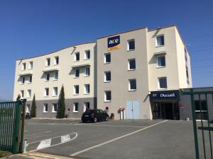 un grand bâtiment blanc avec une voiture garée dans un parking dans l'établissement Ace Hotel Poitiers, à Poitiers