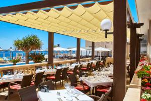 een restaurant met tafels en stoelen met de oceaan op de achtergrond bij Universal Hotel Romantica in Colonia Sant Jordi