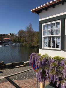 a building with purple flowers in front of a river at A Gosto in Tomar