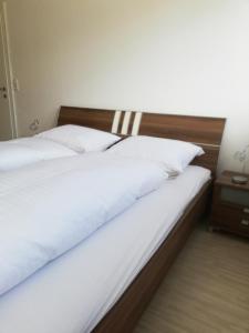 1 cama con sábanas blancas y cabecero de madera en Gemütliches 3 Zimmer Apartment nahe Graz, en Gratkorn