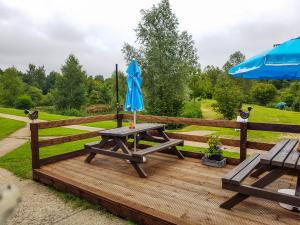 a picnic table with an umbrella on a wooden deck at Colemans Cottage Fishery in Wickham Bishops