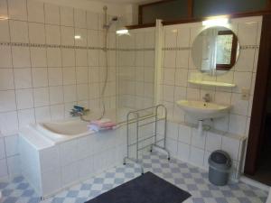 a white tiled bathroom with a sink and a tub and a mirror at Peaceful Nature Stay in Bohon in Barvaux