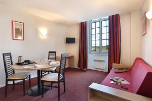 um quarto de hotel com uma mesa e um sofá vermelho em Vacancéole - Les Demeures Champenoises Confort em Épernay