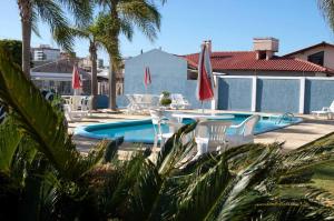 a swimming pool with chairs and a table and umbrellas at HOTEL MAGIA DO MAR in Capão da Canoa