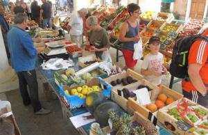 a group of people standing around a market with fruits and vegetables at L’Ile Rousse les pieds dans l’eau in LʼÎle-Rousse +29 photos