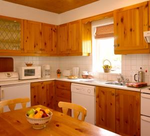 a kitchen with wooden cabinets and a table with a bowl of fruit at The Waterside Cottages in Nenagh