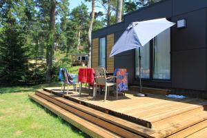 une maison avec une terrasse dotée de chaises et d'un parasol dans l'établissement Camping Domaine du Lac Chambon, à Murol