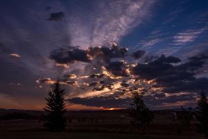 um céu nublado ao pôr-do-sol com árvores num campo em Rocky Ridge Country Lodge em Mountain View