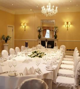 una sala da pranzo con tavoli e sedie bianchi e un lampadario a braccio di New House Country Hotel a Cardiff