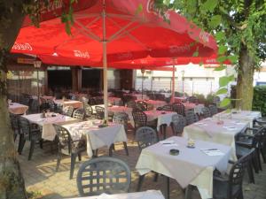 ein Restaurant mit Tischen, Stühlen und roten Sonnenschirmen in der Unterkunft Ristorante Domino in Agno