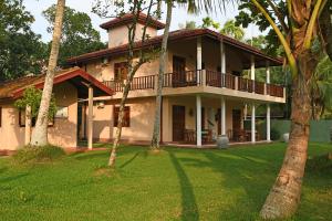 a house with a balcony and a yard with palm trees at Hettimulla River House in Bentota